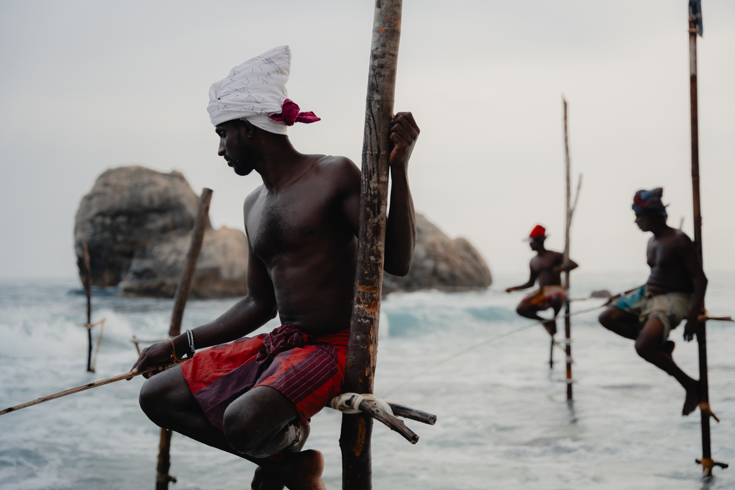 Traditional stilt fishermen in Sri Lanka practicing ancient fishing techniques along the southern coast — iconic cultural scene at sunset near Koggala or Weligama.